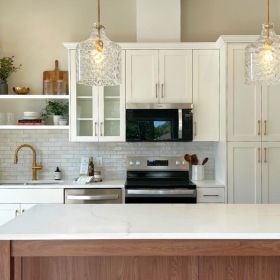 Bright kitchen with white finishes and natural wood accents. Gold hardware and stainless steel appliances.