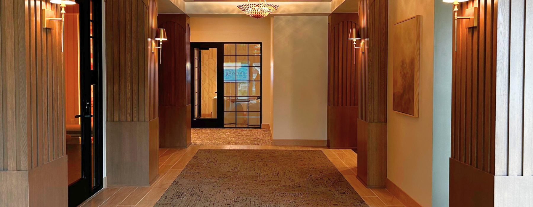 Front entry hallway with long rug and brown pillars lining the hall lit with gold mounted lamps